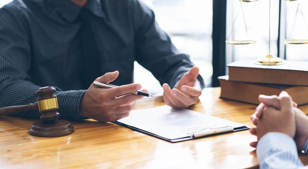 Legal consultation scene with a lawyer discussing documents at a desk, gavel and scales in view.