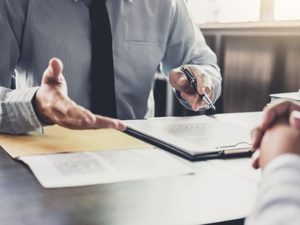 Business meeting with man discussing documents over a desk, pointing with a pen.