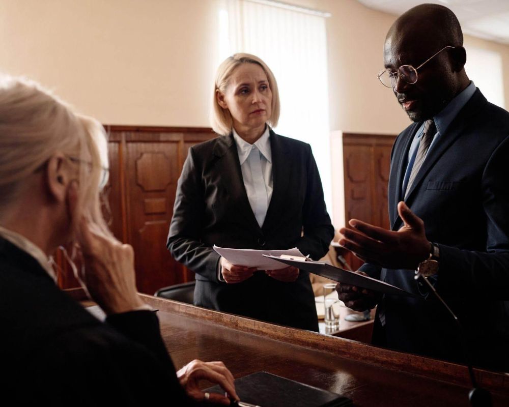 Lawyers discuss case details in a courtroom setting with a judge observing attentively.