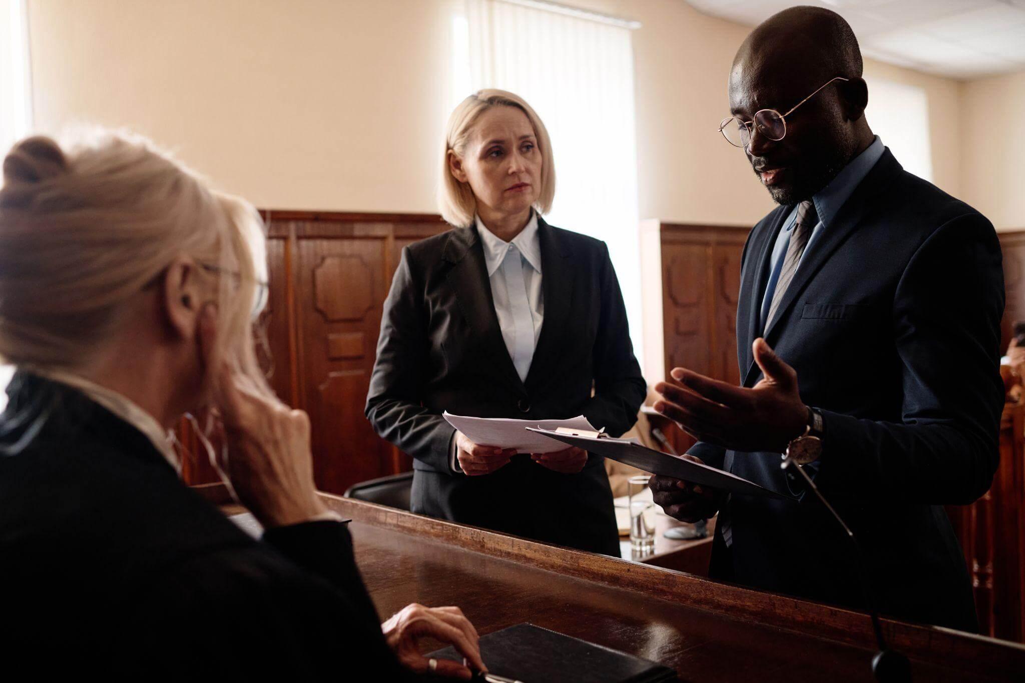 Lawyers discuss case details in a courtroom setting with a judge observing attentively.