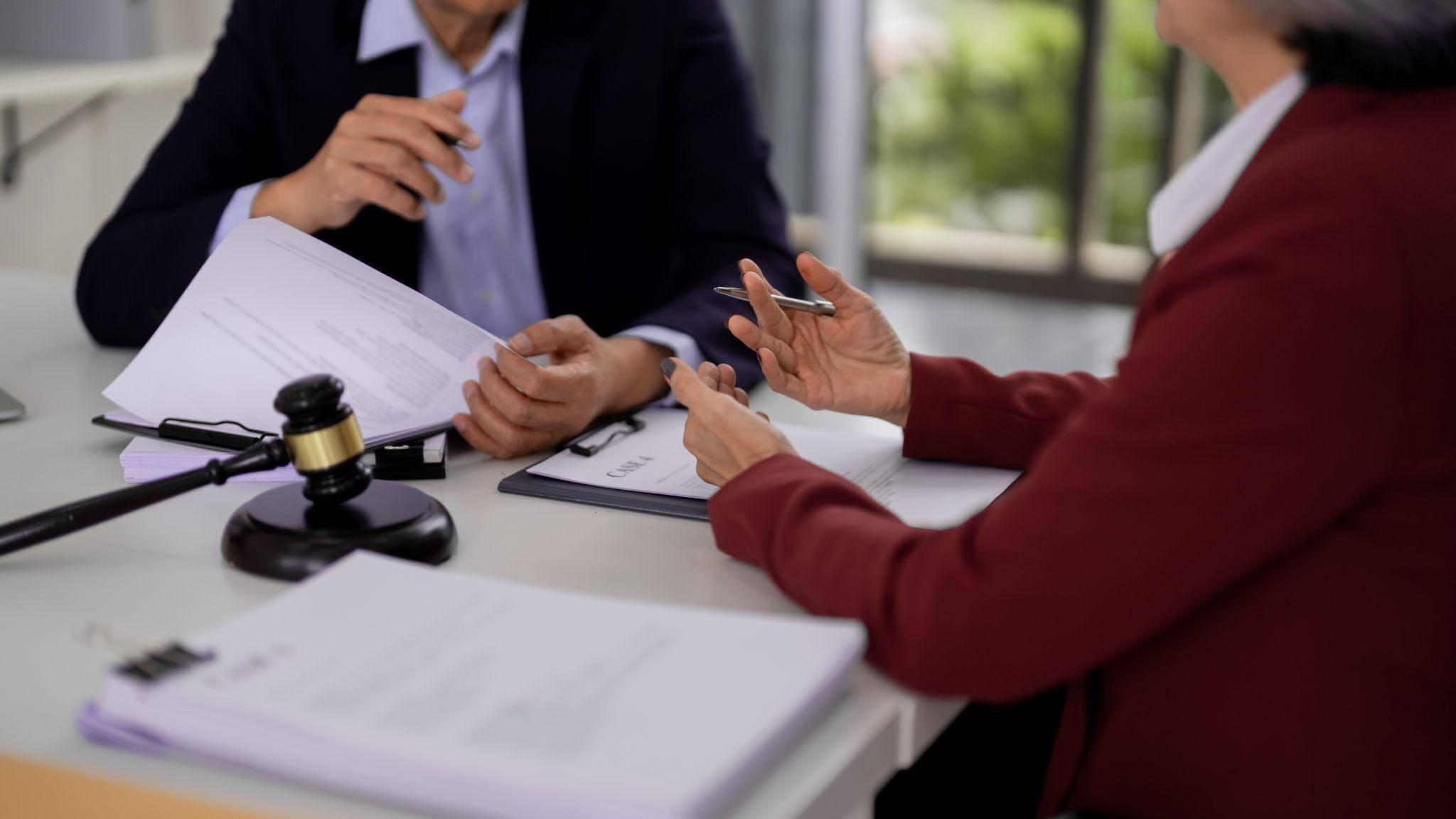 Two professionals reviewing legal documents at a desk with a gavel and paperwork.