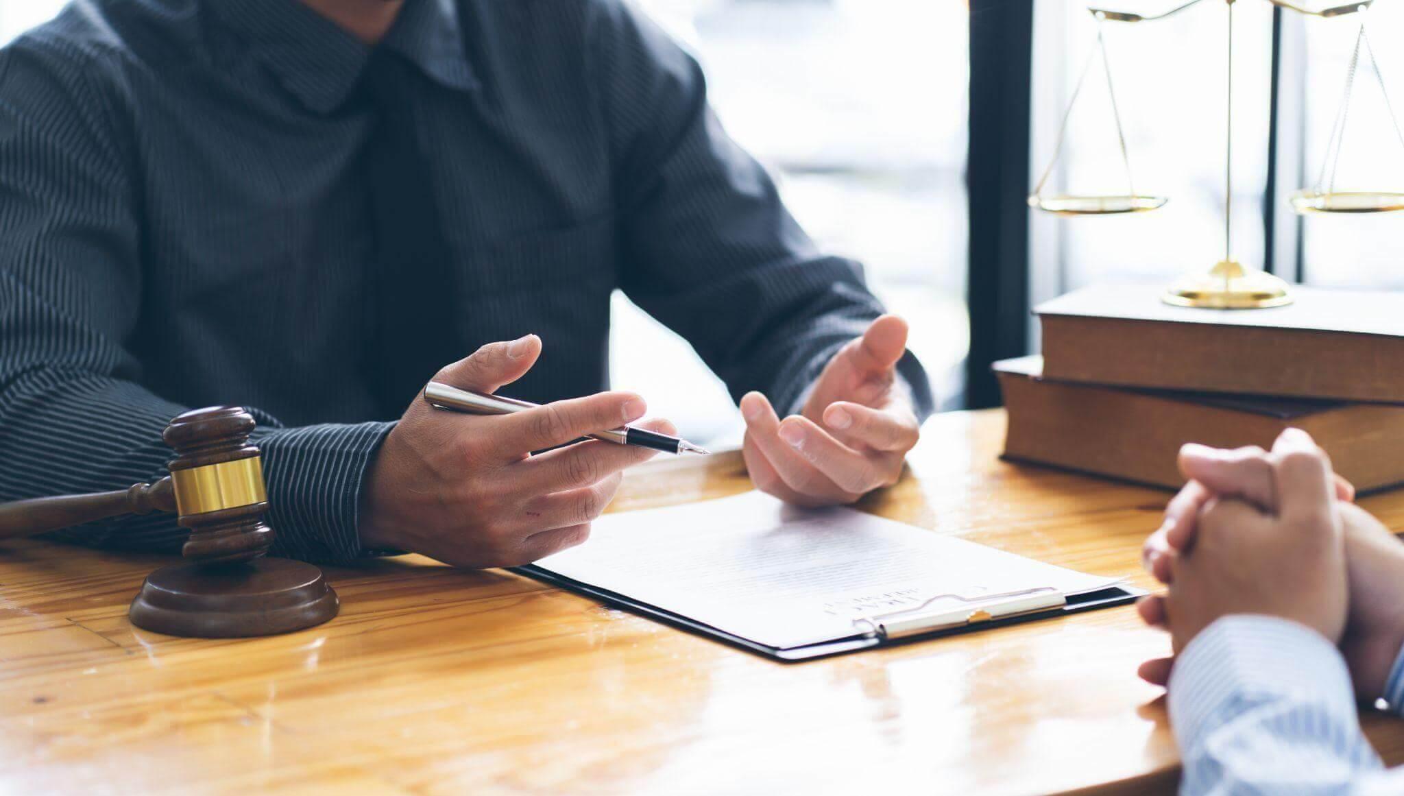 Legal consultation scene with a lawyer discussing documents at a desk, gavel and scales in view.