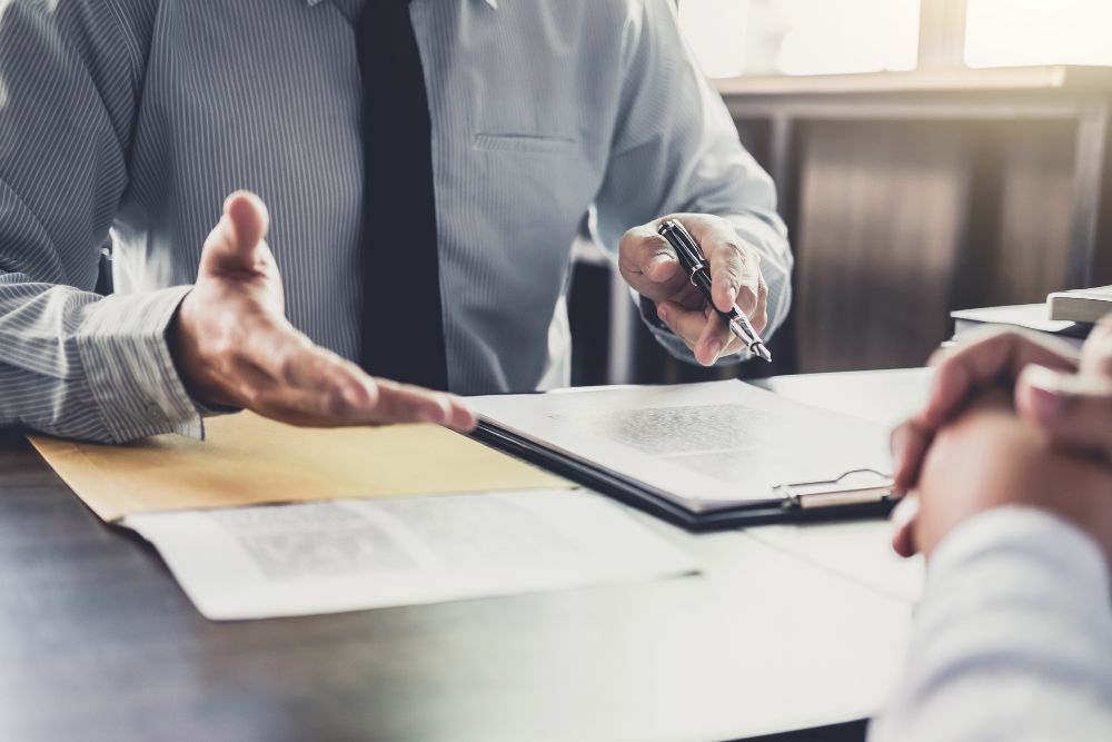 Business meeting with man discussing documents over a desk, pointing with a pen.
